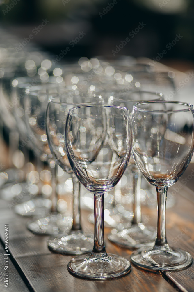 A close-up view of multiple empty wine glasses arranged in rows on a wooden table. A close-up view of multiple empty wine glasses arranged in rows on a wooden table.