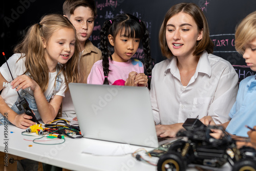 Teacher coding to demonstrate children how to code robots in the STEM class. Children fun to watch how teacher coding with confident only boy in blue shirt taking note with serious look. Erudition.