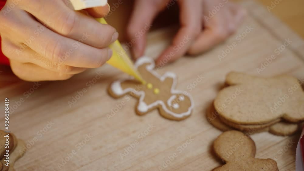 The Woman Adds Yellow Icing to the Gingerbread Man, Meticulously Decorating Each Cookie in Her Festive Red Sweater. The Woman Adds Yellow Icing to the Gingerbread Man, Meticulously Decorating Each Cookie in Her Festive Red Sweater.