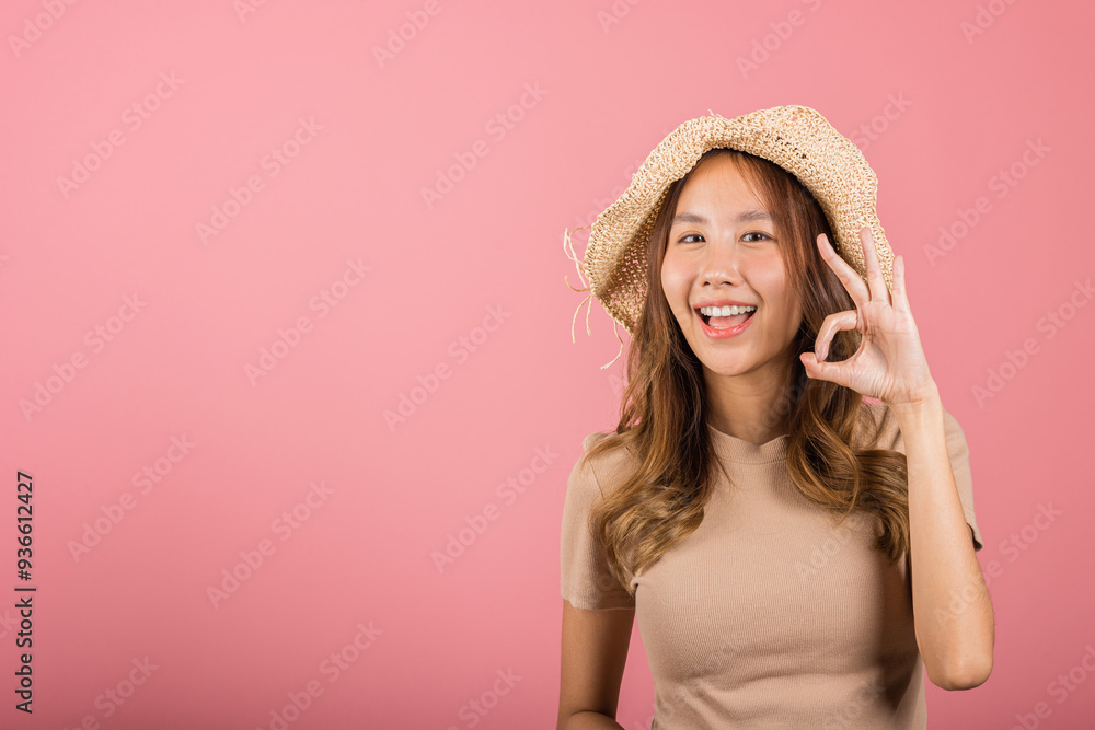 Portrait Asian young woman is smiling with hat holding her hand up in the air, giving the OK sign in studio shot isolated pink background, which gives it a cheerful and positive vibe, excellent sign Portrait Asian young woman is smiling with hat holding her hand up in the air, giving the OK sign in studio shot isolated pink background, which gives it a cheerful and positive vibe, excellent sign