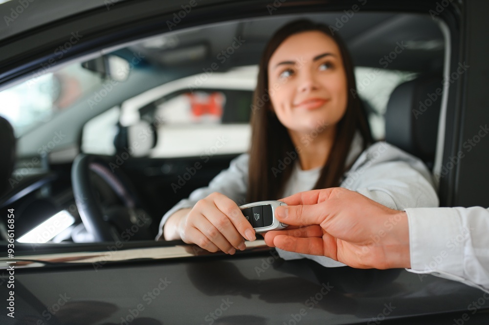 Dealer giving key to cheerful female driver while selling modern red vehicle in dealership Dealer giving key to cheerful female driver while selling modern red vehicle in dealership
