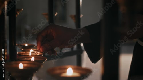 Close up shot of hand of unrecognizable nun lighting up candle with natch in Catholic church