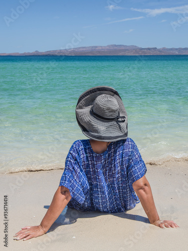 Woman sitting on the shore of the beach sunbathing and watching the crystalline sea of ​​Cortes with the Espiritu Santo island in the background, with the turquoise blue sea of ​​EL TECOLOTE beach. photo