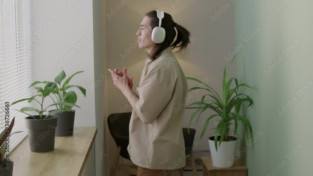 Tilt up shot of young carefree man in headphones listening to music and dancing during day at home Tilt up shot of young carefree man in headphones listening to music and dancing during day at home