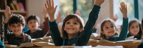 Children smiling and raising their hands in class, seated at desks with books open on the desks. The scene captures happy students engaged during school learning or creative activity photo