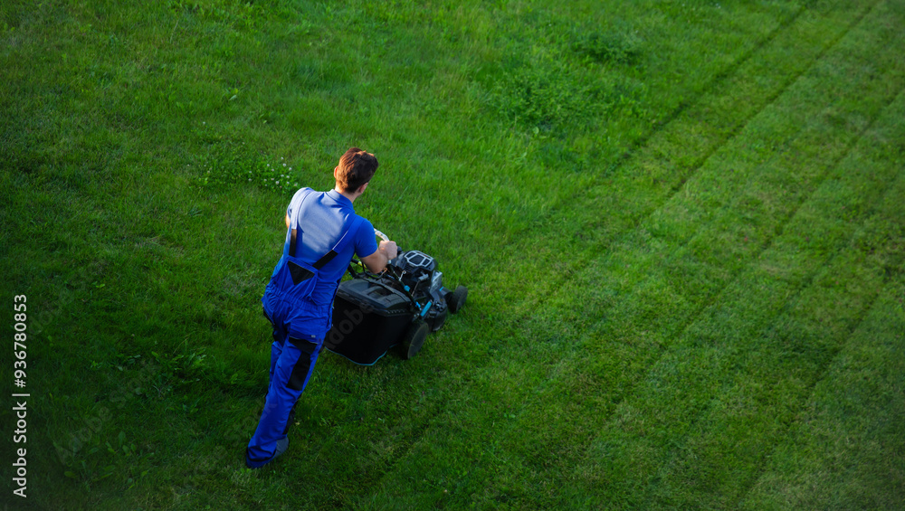 Man in blue overalls is mowing a well-maintained lawn, creating neat, parallel lines in the grass. View from above, captures the precision and care involved in lawn maintenance on a bright, clear day Man in blue overalls is mowing a well-maintained lawn, creating neat, parallel lines in the grass. View from above, captures the precision and care involved in lawn maintenance on a bright, clear day