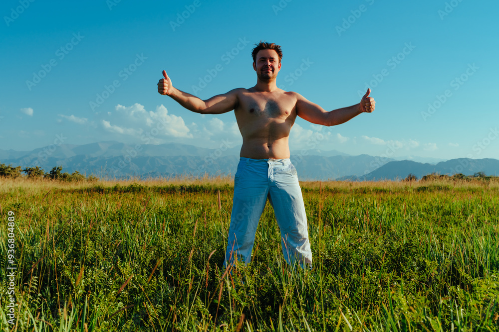 Young strong shirtless man posing in summer meadow on mountains background Young strong shirtless man posing in summer meadow on mountains background