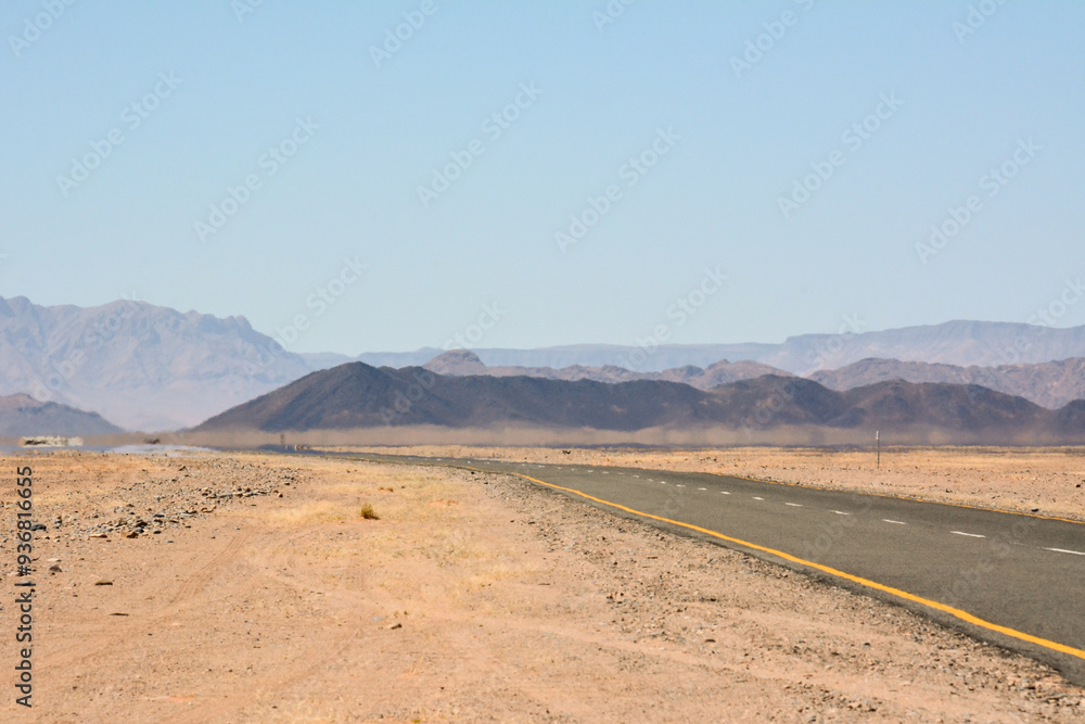 A flat road in the desert in perspective leading to the mountains under the blue sky A flat road in the desert in perspective leading to the mountains under the blue sky