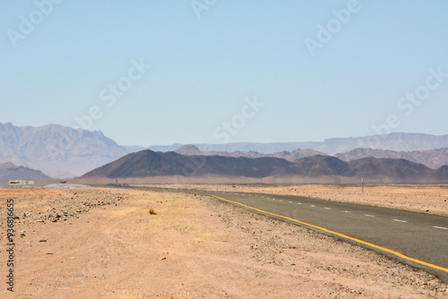 A flat road in the desert in perspective leading to the mountains under the blue sky