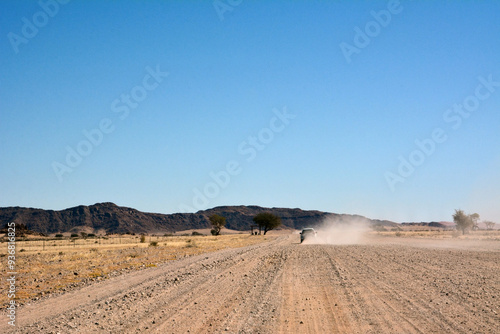 A car drives towards the hills on a dirt road in a desert area in perspective under a clear blue sky