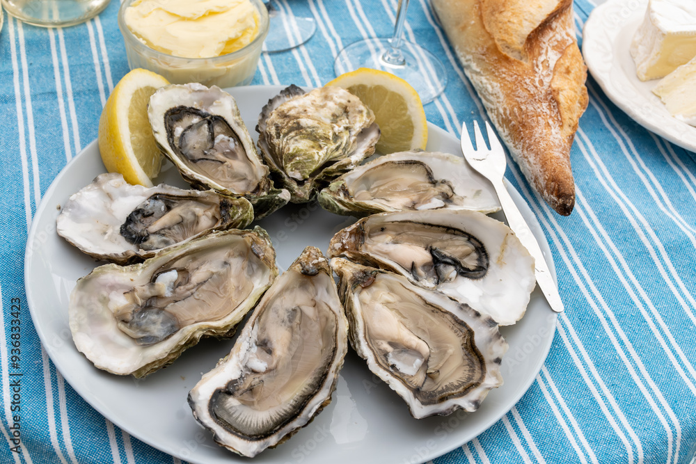 Plate with fresh live oysters with citron, bread, butter and white wine served at restaurant in oyster-farming village, Arcachon bay, Gujan-Mestras port, France Plate with fresh live oysters with citron, bread, butter and white wine served at restaurant in oyster-farming village, Arcachon bay, Gujan-Mestras port, France