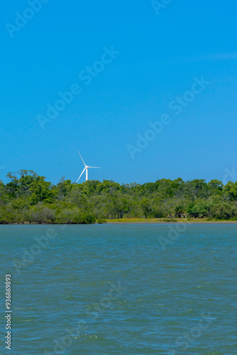 VIEW OF THE JAGUARIBE RIVER IN THE MUNICIPALITY OF FORTIM ON THE EAST COAST OF THE STATE OF CEARÁ WITH A RENEWABLE ENERGY WIND FARM UNDER THE SAND DUNES IN THE BACKGROUND.