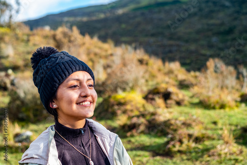 Portrait of a Smiling Latina Woman in Black Hat and Beige Jacket Against Green Hills Background