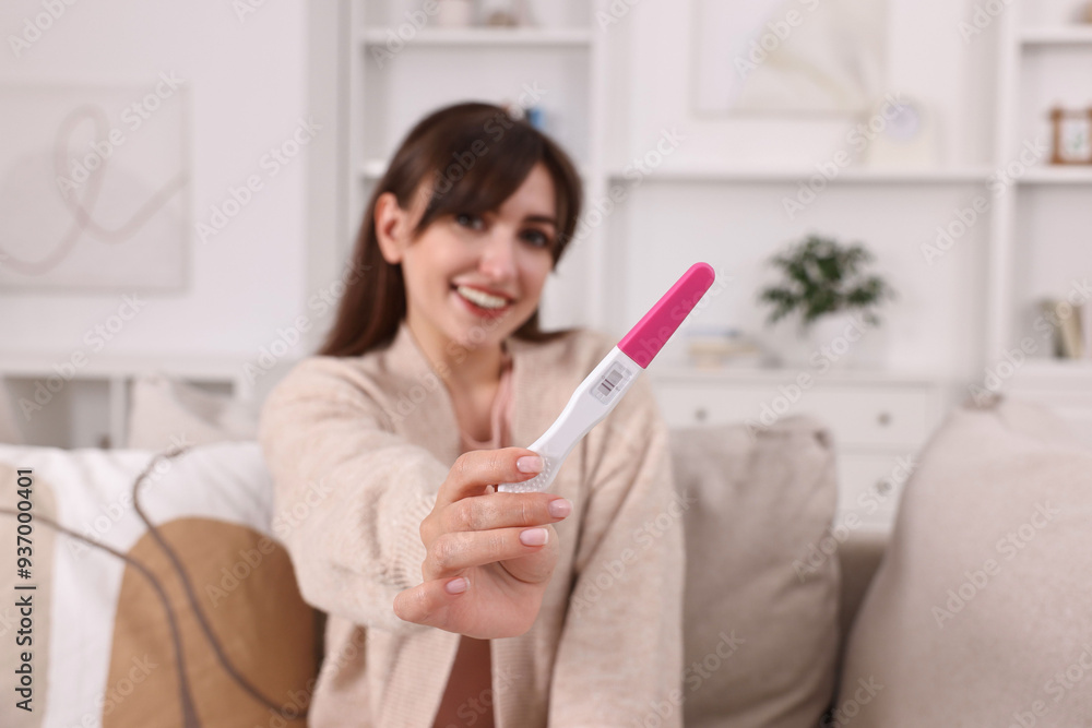 Happy young woman with pregnancy test on sofa at home Happy young woman with pregnancy test on sofa at home