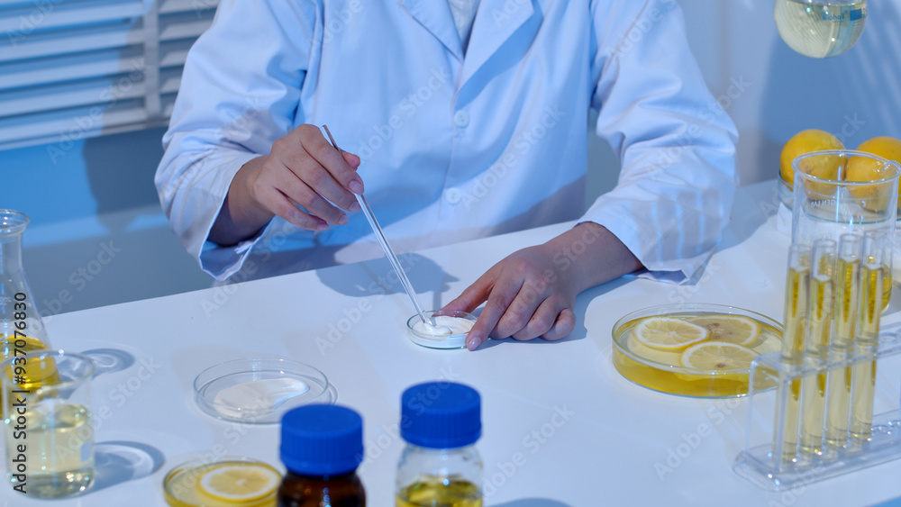 A researcher is stirring cream in a petri dish, surrounded by a dish of cream and lemon ingredients in glassware on a table. Laboratory background with blue light A researcher is stirring cream in a petri dish, surrounded by a dish of cream and lemon ingredients in glassware on a table. Laboratory background with blue light