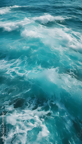 Aerial view of turquoise ocean waves crashing gently, creating white foam. The water is clear and vibrant, showcasing various shades of blue and green.