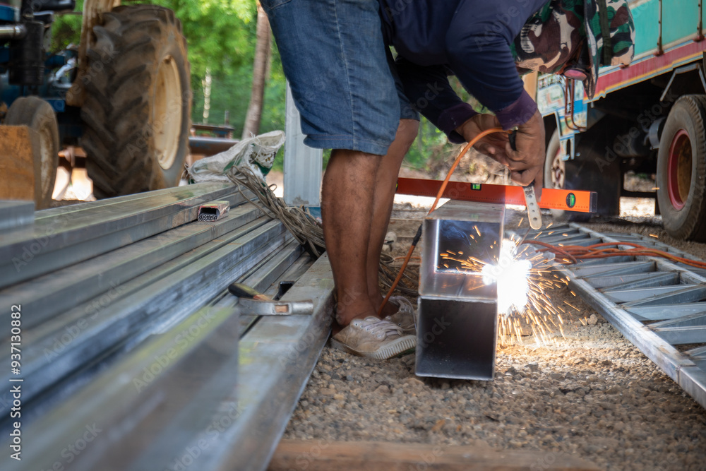 A man is sitting on the ground and working on a metal structure. A man is sitting on the ground and working on a metal structure.