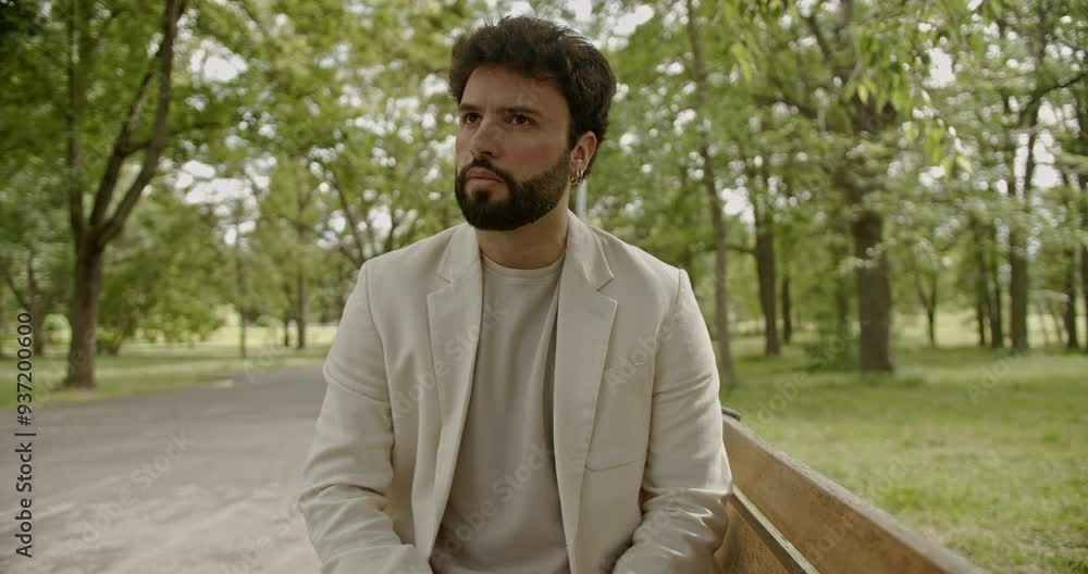 A young businessman with a worried expression sits on a bench in a park, deep in thought A young businessman with a worried expression sits on a bench in a park, deep in thought