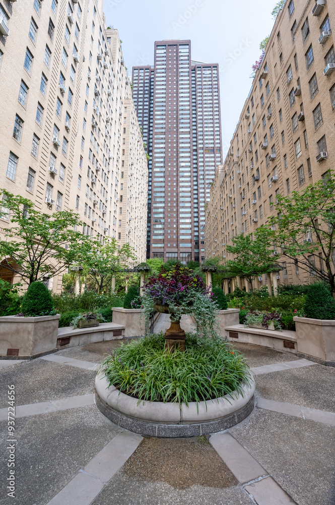 Obraz premium This elegant urban courtyard in New York City features meticulously landscaped gardens surrounded by classic brick buildings. The lush greenery and peaceful setting create a serene retreat amidst the 