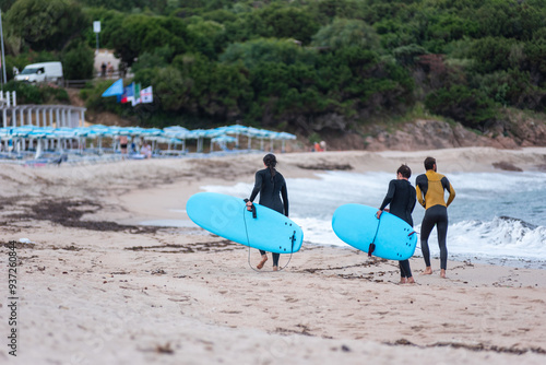 Canvas Print A trio of young surfers, clad in wetsuits and carrying their boards, walk together after emerging from the ocean