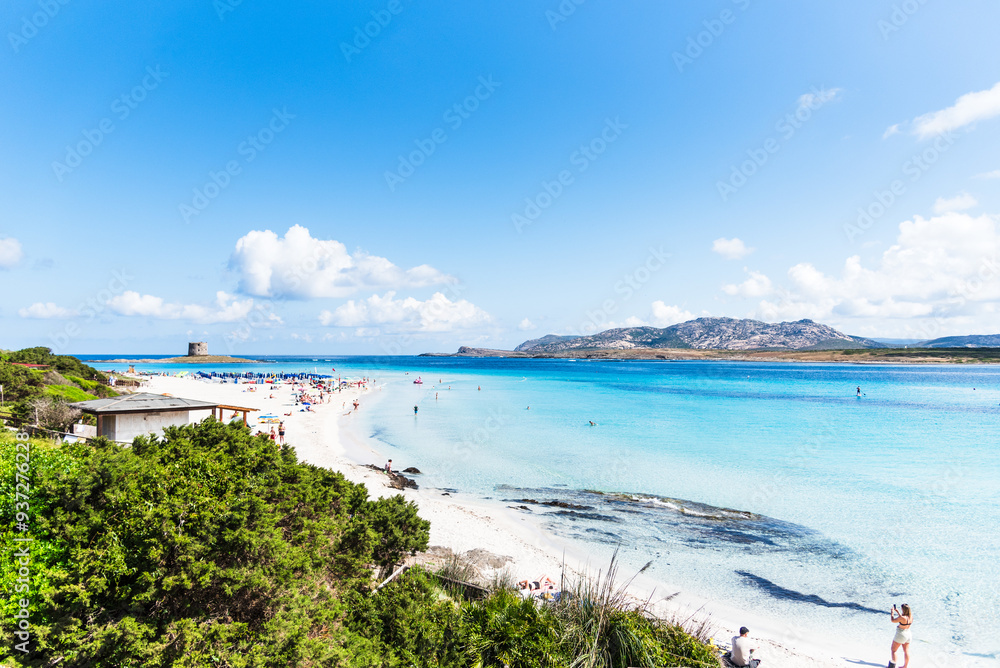Obraz premium An elevated view reveals the vibrant life of La Pelosa beach, where people dot the shore, blending with the brilliant blue waters of the bay.
