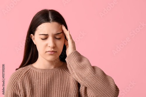 Beautiful young woman suffering from headache on pink background