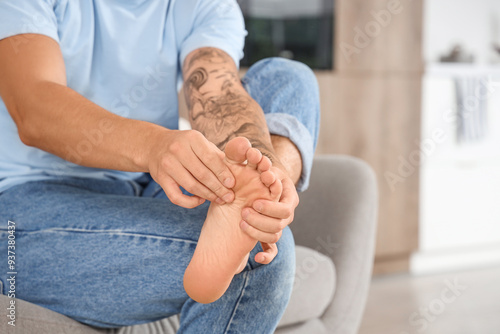 Young man with flat feet sitting on sofa at home, closeup photo