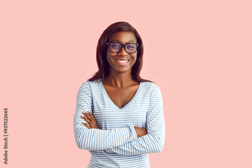 Portrait of happy woman in casual clothes and glasses. Young African American girl in eyeglasses and light blue long sleeve shirt holding arms crossed and smiling isolated on pastel pink background Portrait of happy woman in casual clothes and glasses. Young African American girl in eyeglasses and light blue long sleeve shirt holding arms crossed and smiling isolated on pastel pink background