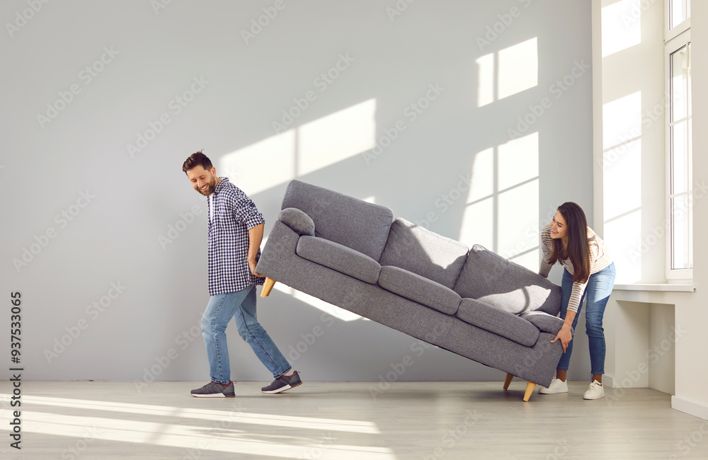 © Studio Romantic - Young family couple moving furniture in their new house or apartment. Man and woman buy a new sofa and put it in the living room. Happy husband and wife moving a new gray couch inside their apartment