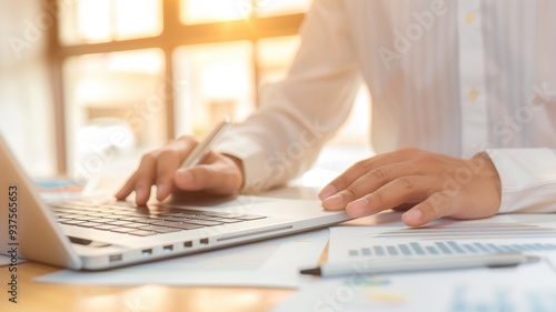 Close-up of a person's hand working on a laptop in a bright environment, with soft sunlight illuminating the workspace.