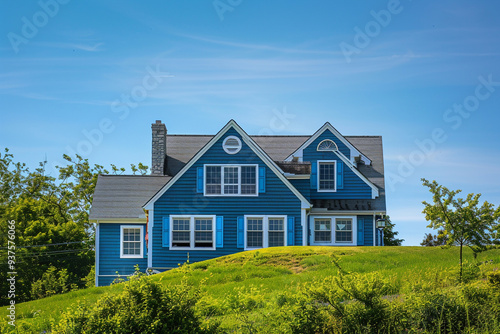 From a distant hill, the serene sky blue home with traditional windows and shutters blends seamlessly into the suburban landscape, offering a picturesque scene under the clear blue sky.