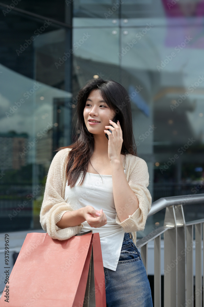 Fototapeta premium Portrait of beautiful woman with shopping bags talking on mobile phone outside shopping mall