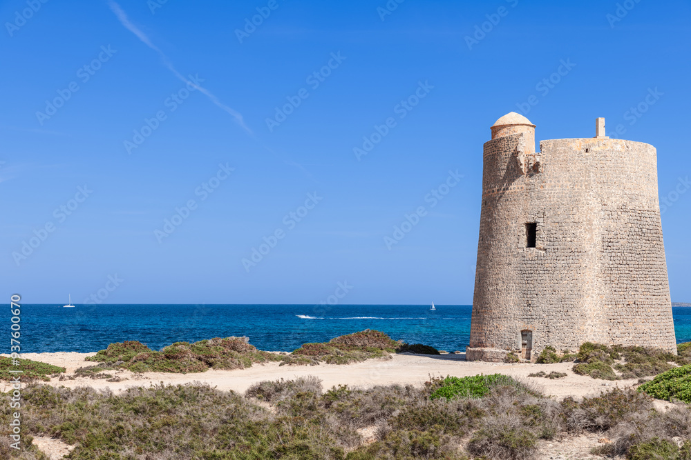 Ancient Torre de ses Portes on Ibiza coast with boats and sailboats dotting the turquoise Mediterranean Sea. The clear blue sky adds to the serene coastal scene of this Spanish island Ancient Torre de ses Portes on Ibiza coast with boats and sailboats dotting the turquoise Mediterranean Sea. The clear blue sky adds to the serene coastal scene of this Spanish island