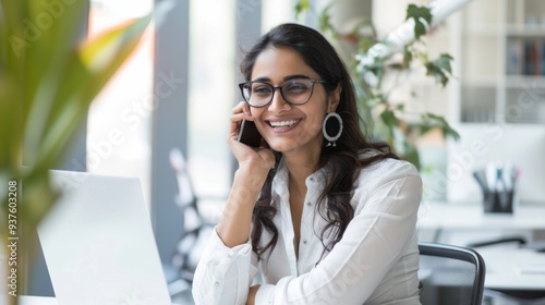 With a warm smile, an attractive Indian woman engages in a lively phone conversation, surrounded by greenery and a contemporary workspace, radiating confidence and joy Free Download With a warm smile, an attractive Indian woman engages in a lively phone conversation, surrounded by greenery and a contemporary workspace, radiating confidence and joy - GFXLoad
