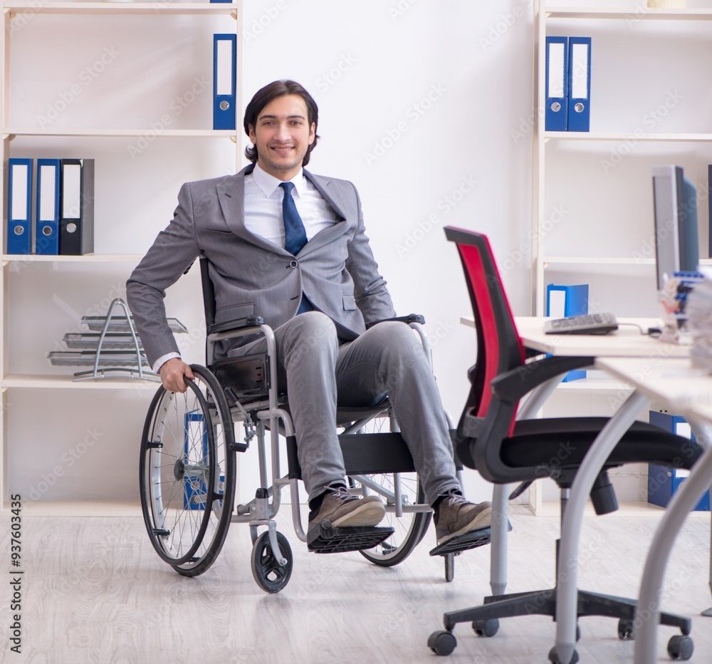 Young handsome employee in wheelchair working in the office Young handsome employee in wheelchair working in the office