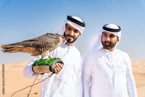 Two middle-eastern emirati men wearing arab kandura holding falcon in the desert