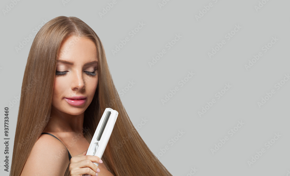 Brunette fashion model with brown shiny straight haistyle portrait. Cute woman with straightening iron in her hand on gray studio background Brunette fashion model with brown shiny straight haistyle portrait. Cute woman with straightening iron in her hand on gray studio background