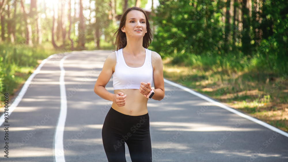 Fototapeta premium Female runner athlete does workout runs, uses fitness watch