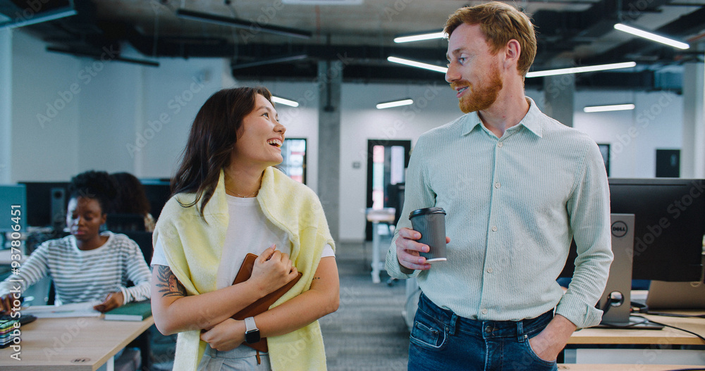 Cute couple walking through their workspace. Casually talking and smiling while enjoying conversation. Discussing possible plans for evening during coffee break. Modern room. Many desks with monitors. Cute couple walking through their workspace. Casually talking and smiling while enjoying conversation. Discussing possible plans for evening during coffee break. Modern room. Many desks with monitors.