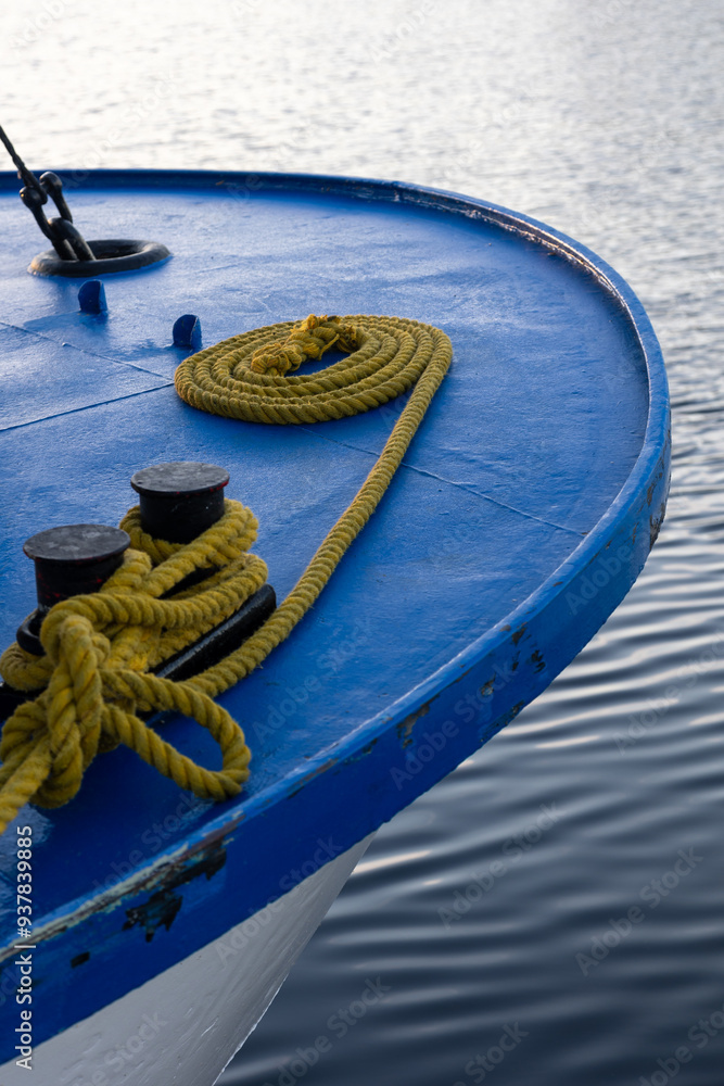 Fototapeta premium Close-up of a blue boat's edge with coiled rope and cleats on a calm water surface during sunset