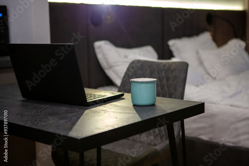 Hotel room with bed and comfort zone for work with laptop. Black furniture in interior and cup of drink on the desk