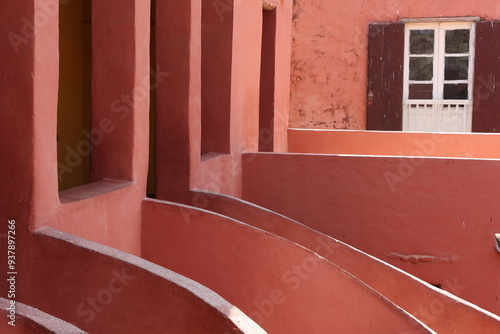 Vue d'un détail de l'escalier de couleur orangée de la maison des esclaves de l'île de Gorée au Sénégal. Rampe de forme incurvée. Architecture coloniale. Bâtiment rénové et coloré. Avril 2024.