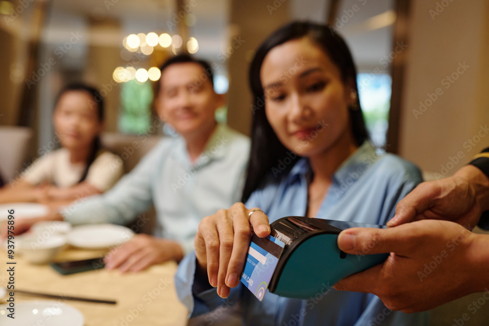 Woman paying with credit card while waiter holding the terminal after dinner in the restaurant Woman paying with credit card while waiter holding the terminal after dinner in the restaurant