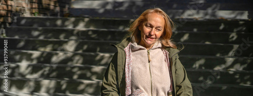 An elderly smiley wooman feels happy, walks in a park outdoors in the rays of a sun.