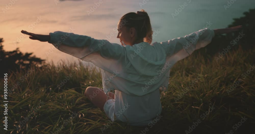 Young woman meditates and practices yoga on a hill at sunset, feeling free and connected to nature