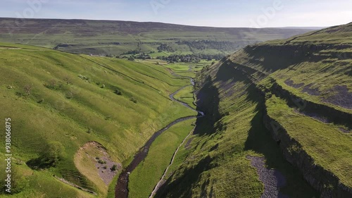 A lush landscape capturing the essence of Arncliffe with its meandering river through the green valley, framed by slopes and sunlight shadows photo