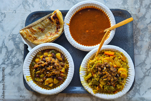 A tray full of Moroccan vegan food features tomato soup, potato stew, couscous, beans, msemen flatbreads served with single-use plates and cutlery.