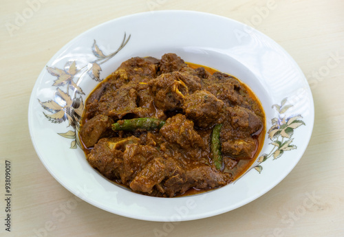 Delicious mutton curry in a white plate on a wooden background. Mutton bhuna is a popular, flavorful, and spicy traditional Bangladeshi dish. photo