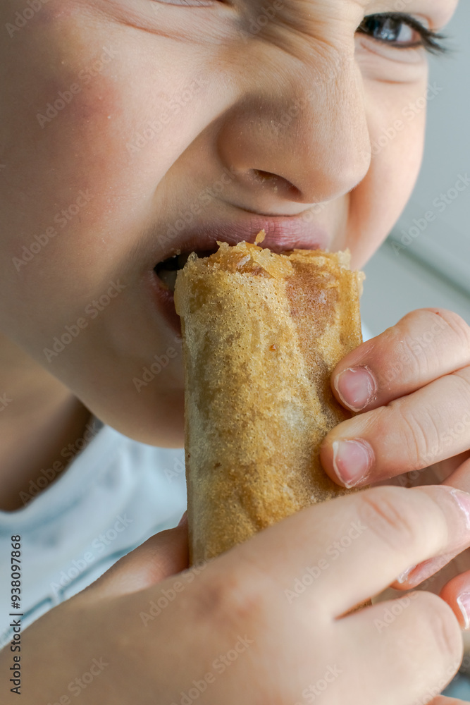 A kid eating an Algerian Bourek or Brik. Close up view of the child holding the Burek and making a face expression grimace while biting it. A kid eating an Algerian Bourek or Brik. Close up view of the child holding the Burek and making a face expression grimace while biting it.