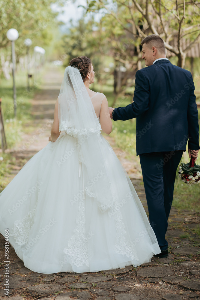 A bride and groom are walking down a path in a garden. The bride is wearing a white dress and a veil, while the groom is wearing a suit. They are holding hands and appear to be happy and in love A bride and groom are walking down a path in a garden. The bride is wearing a white dress and a veil, while the groom is wearing a suit. They are holding hands and appear to be happy and in love